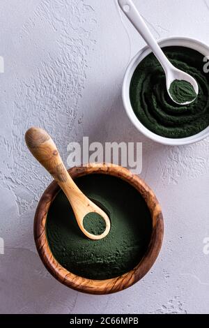 Poudre de chlorelle ou de spiruline dans un bol en bois et dans un bol en porcelaine par le dessus. Les bols sont dotés de cuillères assorties. Alimentation saine et diétine Banque D'Images
