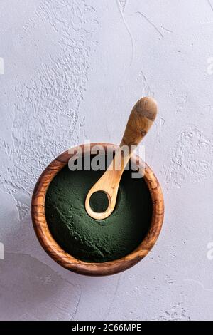 Poudre de chlorelle verte ou de spiruline dans un bol en bois naturel brun par le dessus et petite cuillère pleine sur lui. Alimentation saine et alimentation saine Banque D'Images
