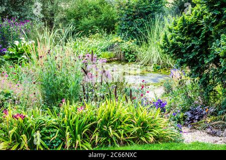 Chemin de gravier à travers la végétation luxuriante de jardin menant à un étang. Banque D'Images