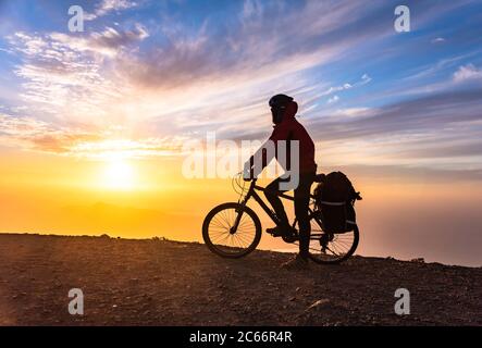 Mountain Bicycle Rider avec sac à dos voyage au-dessus de l'arrière-plan sunrise, Lanzarote Canary Island Banque D'Images