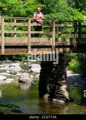 Femme debout sur une passerelle au-dessus de Hoar Oak Water, Watersmeet, Devon, Royaume-Uni Banque D'Images