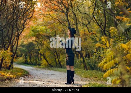 une femme avec une belle figure dans un chapeau noir se tient latéralement dans le parc et pose pour une séance photo Banque D'Images