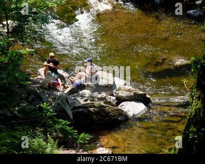 Un couple d'âge moyen s'est assis sur des rochers à côté de la rivière East Lyn pour un pique-nique, à Devon, au Royaume-Uni Banque D'Images