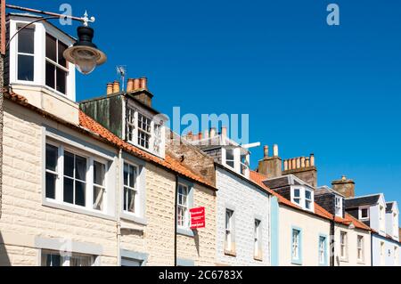 Une rangée de cottages en terrasse sur le front de mer à Mid Shore Pittenweem dans East Neuk of Fife, un avec un panneau à vendre. Banque D'Images