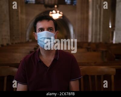 Portrait horizontal d'un homme portant un masque chirurgical assis et priant dans une église Banque D'Images