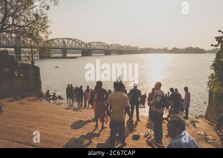 Dakshineswar Kali Mandir Temple Ghat sur la rive de Holi Ganges. Heure du coucher du soleil. Des gens bondés qui font des rituels le soir. Vue sur le soleil avec garde-corps Banque D'Images