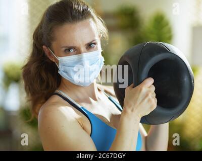 La vie durant la pandémie du coronavirus. Une femme de 40 ans en bonne santé dans des vêtements de fitness avec deux boules de médecine de préhension. Banque D'Images