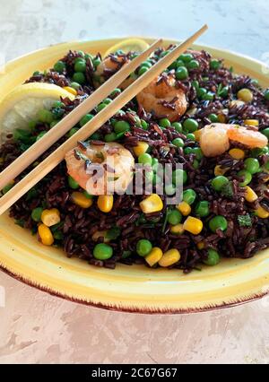 Concept de la cuisine d'été. Salade de riz noir froid avec maïs, pois, crevettes et citron sur assiette jaune. Une alimentation saine. Vue de dessus. Banque D'Images