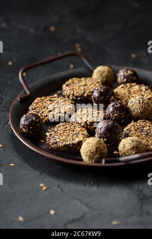 Bonbons végétaliens crus sains. Bouchées d'énergie faites maison avec des graines de lin dans un plateau métallique sur fond noir espace de copie Banque D'Images