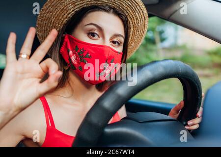 Une femme conducteur assis en voiture portant un masque de protection pendant une pandémie de coronavirus. Une fille montre un panneau ok cool Banque D'Images