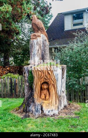 La tronçonneuse sculpte sur une souche d'arbre, de ce qui peut être un ours et un aigle dans une cour résidentielle de Granite Falls, Washington. Banque D'Images