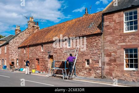 Deux personnes pointent et réparent une vieille maison dans le village de Stenton, East Lothian, Écosse, Royaume-Uni. Banque D'Images