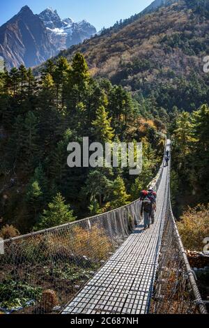 Des porteurs transportent du matériel sur un pont sur la piste jusqu'au camp de base de l'Everest. Banque D'Images