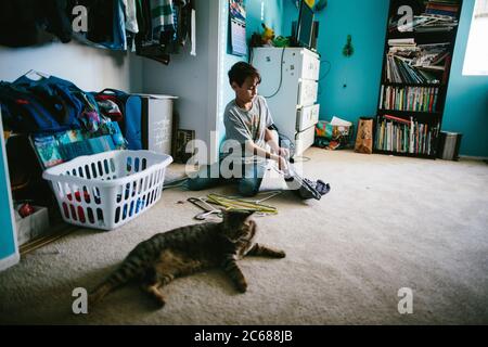 Garçon dans sa chambre en mettant une chemise sur un cintre avec son chat à proximité Banque D'Images
