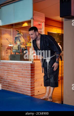 Homme de karaté posant avec un arc pour accéder sur le tatami portant un kimono noir Banque D'Images