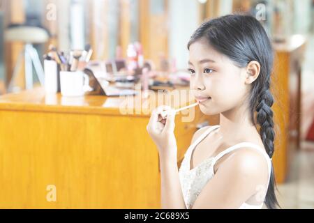 Une jeune fille asiatique à cheveux longs est en utilisant le rouge à lèvres pour appliquer le maquillage de lèvres pendant une leçon de maquillage. Banque D'Images