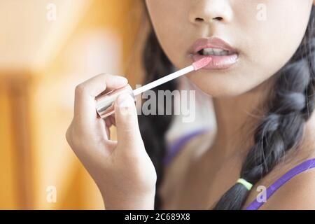 Une jeune fille asiatique à cheveux longs est en utilisant le rouge à lèvres pour appliquer le maquillage de lèvres pendant une leçon de maquillage. Banque D'Images