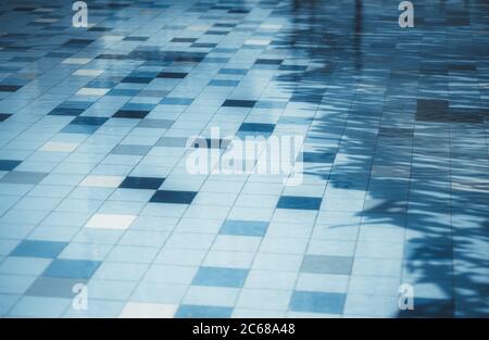 Une surface de fond carrelée d'une piscine de rue avec de l'eau de couleur bleue classique, avec quelques carreaux d'un ton différent et une ombre diagonale sur la droite Banque D'Images