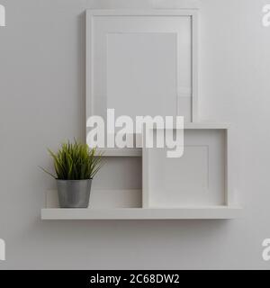 Vue rapprochée de l'intérieur moderne de la maison avec des cadres de maquette et pot de plante au-dessus de la tablette blanche sur le mur blanc Banque D'Images