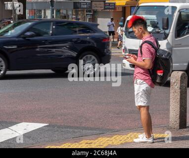 Homme en rouge style mohawk attendant de traverser la rue, Shibuya, Tokyo, Japon Banque D'Images