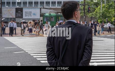 Employé de bureau masculin en costume d'affaires attendant de traverser la route, Shibuya, Tokyo, Japon. Banque D'Images