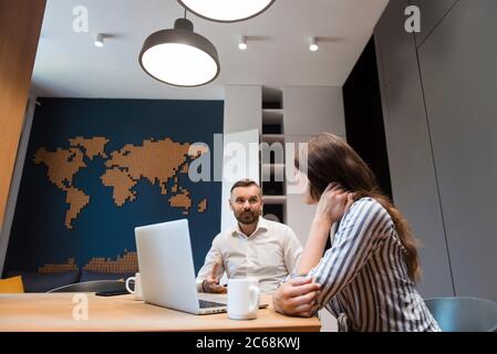 Homme assis au bureau avec un ordinateur portable et parlant à une femme
