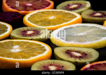 Tranches rondes d'oranges rouges et jaunes et de kiwis rouges sur fond noir. Banque D'Images