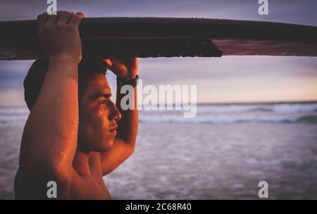 Gros plan d'une tenue de surfeur sûre et sérieuse sa planche de surf au-dessus de sa tête regardant la mer pendant Un magnifique coucher de soleil dans le bin Equateur Banque D'Images