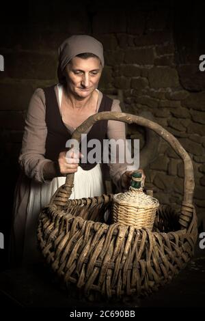 Femme en robe paysanne médiévale contrôler son panier alimentaire dans les caves d'un château médiéval authentique, libéré de la propriété en France Banque D'Images