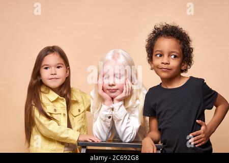 portrait de trois timides et calmes divers enfants isolés en studio. albino fille avec la peau blanche et la couleur des cheveux stand s'ennuient, son africanamerican et l'europe Banque D'Images