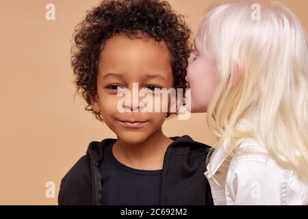 portrait des enfants doux ayant secret isolé en studio, de beaux enfants de diverses nationalités se tiennent ensemble, albino fille avec des cheveux blonds disent Banque D'Images