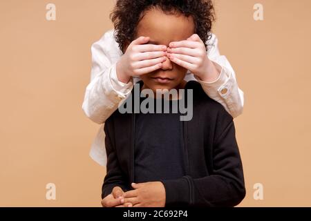 ne identifie pas l'enfant fille avec la peau pâle fermant les yeux du garçon africain du dos, jeu deviner qui. enfants divers, différentes nationalités Banque D'Images