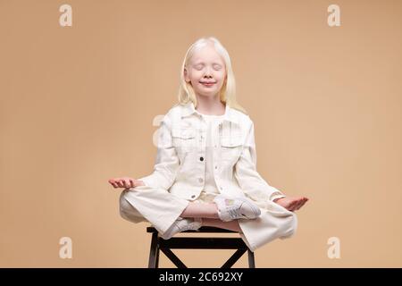 enfant albinos extraterrestre inhabituel assis dans la pose de yoga isolé en studio, garder calme et rester patient. dans la pose de lotus Banque D'Images