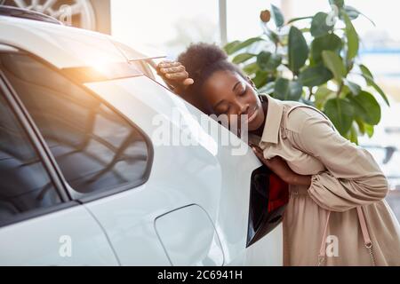 belle femme afro rêve de nouvelle voiture, jeune femme est venue voir des automobiles, faire l'achat. femme est penchée sur la voiture blanche luxueuse, souriant Banque D'Images