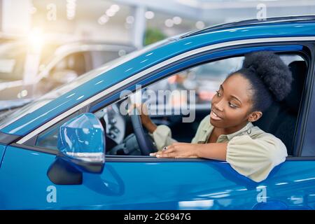 belle femme afro rêve de nouvelle voiture, jeune femme est venue voir des automobiles, faire l'achat. Banque D'Images