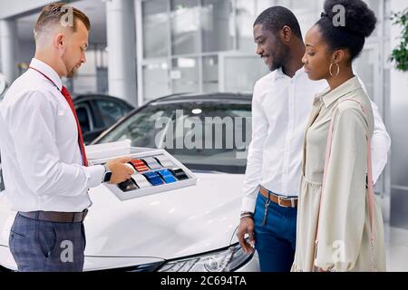 les jeunes clients africains choisissent la couleur de la voiture dans la concession, ils vont faire l'achat, le consultant les aide avec le choix, donne la palette de couleurs Banque D'Images