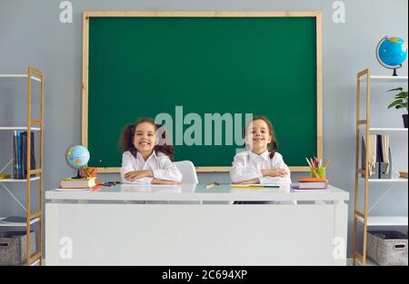 Retour à l'école. Des petites filles d'école positives sont assises à la table dans la classe. Banque D'Images