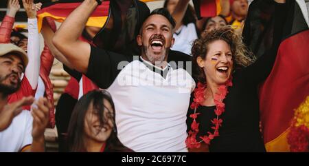 Groupe de fans de football multiethniques qui applaudissent de la zone des fans du stade. Les supporters allemands célèbrent la victoire de leur équipe nationale. Banque D'Images