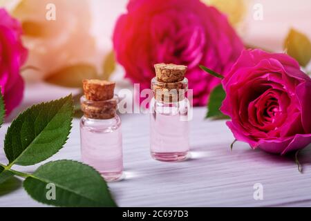 eau de rose parfumée ou huile essentielle dans des bouteilles de verre avec des fleurs sur une table en bois Banque D'Images