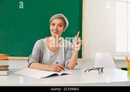 Un enseignant supérieur positif enseigne un doigt vers le haut enseignant les élèves dans une classe scolaire. Banque D'Images