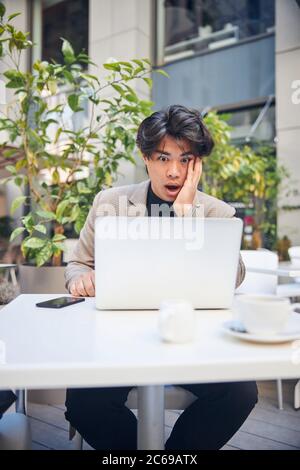 Un jeune homme choqué utilise son ordinateur portable dans un café en plein air Banque D'Images