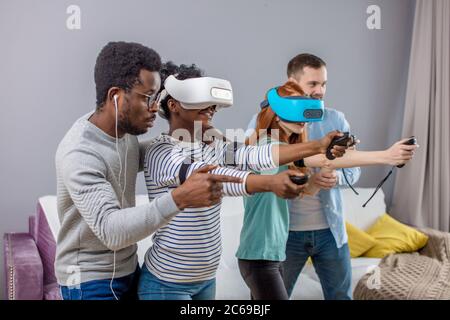 Groupe multiculturel d'amis à jouer à des jeux vidéo portant des lunettes de réalité virtuelle avec les contrôleurs, les femmes d'essayer de jouer et faire de petits amis conseils pratiques Banque D'Images