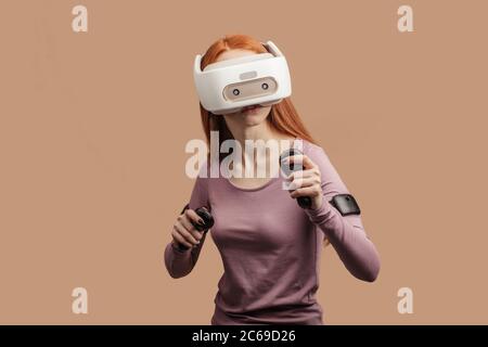 Méconnaissable young female with ginger hair gesturing with hands in active, l'exploration de la réalité virtuelle 3D portable avec casque lors du comité permanent Banque D'Images