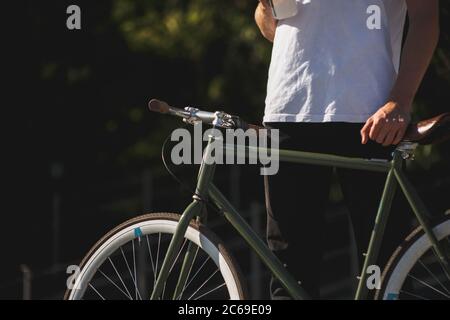Gros plan de l'homme corps en t-shirt blanc tenant vélo . Corps homme debout avec vélo vert foncé classique Banque D'Images