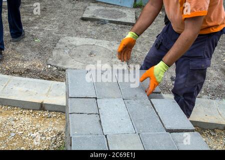 Le maître pose de nouvelles briques de béton pour le trottoir sur la pile. Les briques ont été préparées pour la pose d'un nouveau sentier. Banque D'Images