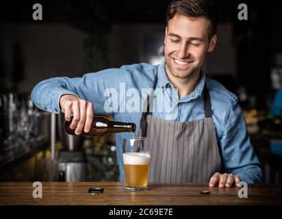 Le barman verse un verre de bière. Un homme souriant et charmant avec une bouteille au bar Banque D'Images