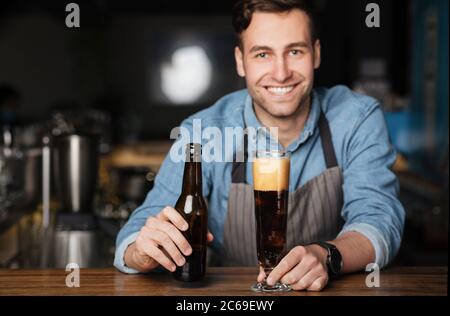 Bière fraîche pour le client. Le barman souriant verse une boisson sombre dans un verre haut Banque D'Images