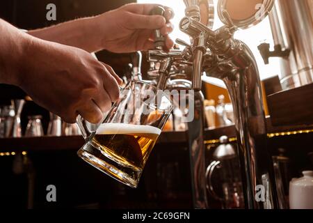 Barman de travail. Le barman verse de la bière à la pression dans une tasse en verre à l'intérieur du pub Banque D'Images