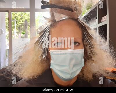 La femme blonde avec des boucles au coiffeur obtient ses cheveux teints avec le protège-bouche Banque D'Images