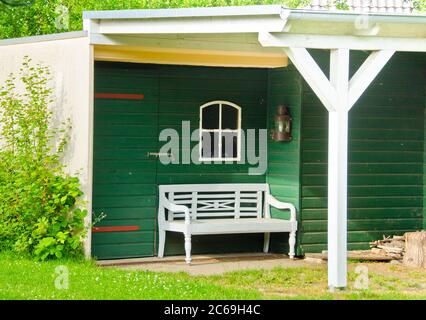 Un petit hangar en bois et vert clair, un jardin, avec un banc quelques outils autour Banque D'Images